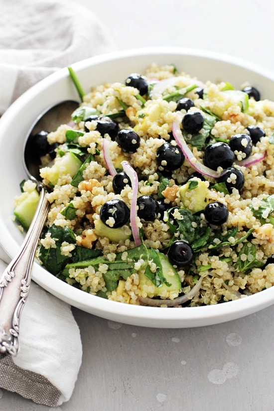 A white bowl filled with Summer Quinoa Salad with a serving spoon in the dish.