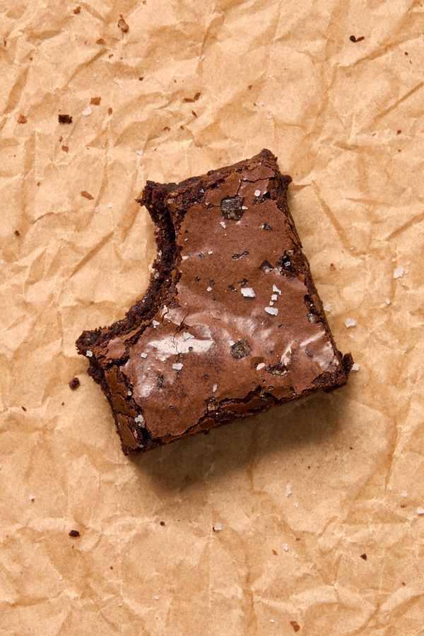 One Dairy Free Chocolate Brownie on parchment with a bite taken out.