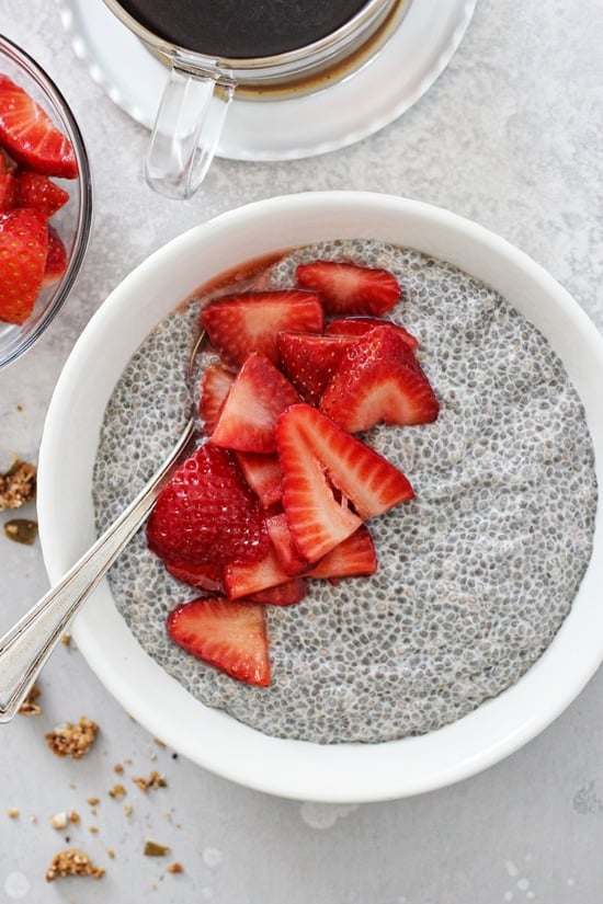 A white bowl filled with Strawberry Chia Pudding and a cup of coffee to the side.