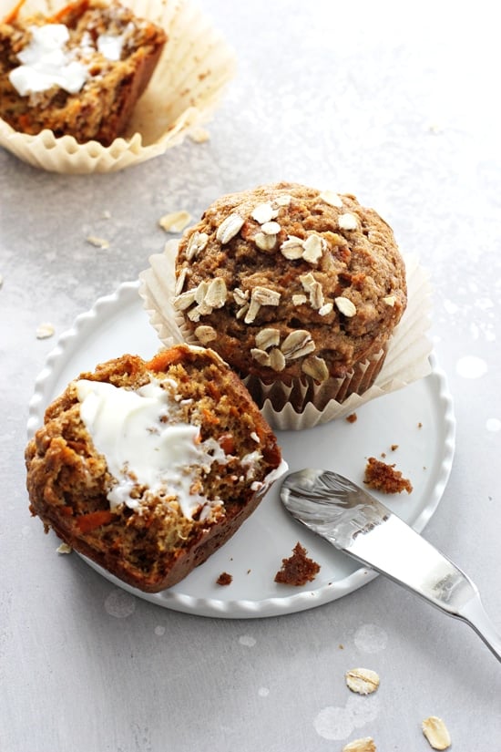 Two Carrot and Banana Muffins on a white plate with butter smeared on one.