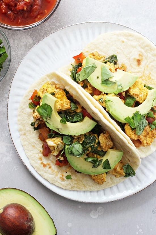 Two Healthy Breakfast Tacos on a white plate with avocado and salsa to the side.