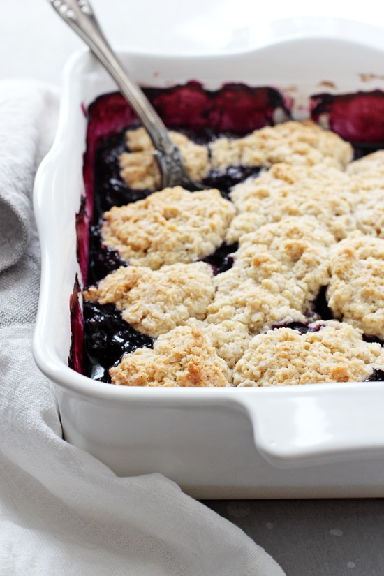 A white baking dish filled with Vegan Berry Cobbler with a serving spoon in the pan.