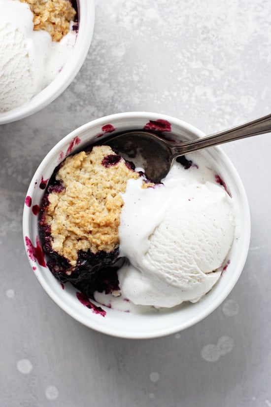 Two ramekins of Vegan Blueberry Cobbler with ice cream and a spoon in one dish.