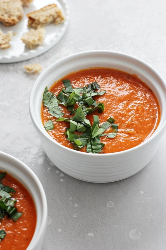 A white bowl filled with Dairy Free Tomato Soup with bread to the side.