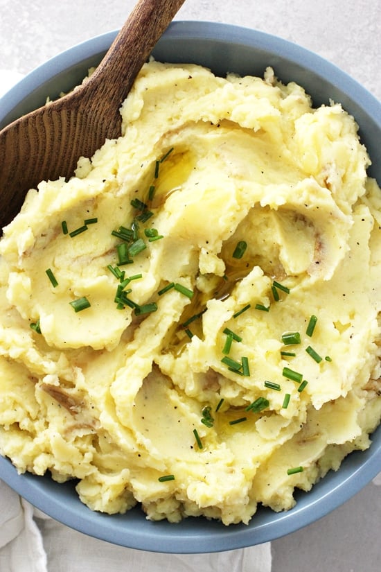 A blue bowl filled with Vegan Mashed Potatoes with a wooden spoon in the dish.