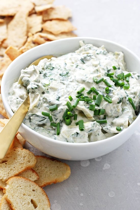 A white bowl filled with Dairy Free Spinach Artichoke Dip and a gold spoon.