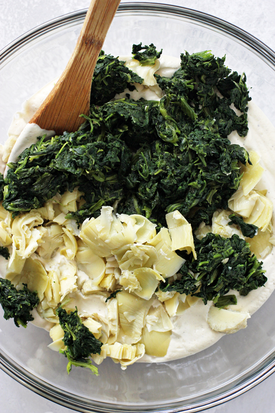 Cashew cream in a mixing bowl with chopped spinach and artichokes.