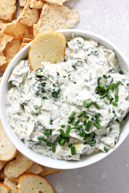 Vegan Spinach Artichoke Dip in a white bowl with chips scattered around.