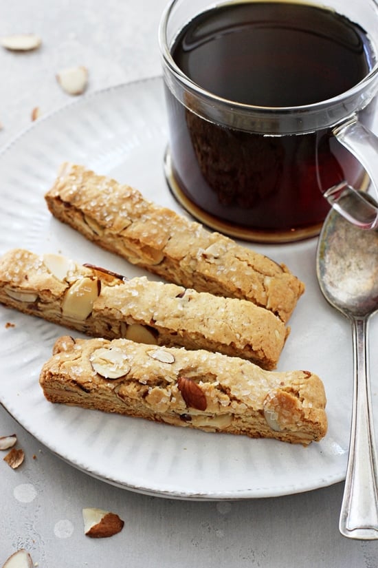 Three Vegan Almond Biscotti on a plate with a cup of coffee.