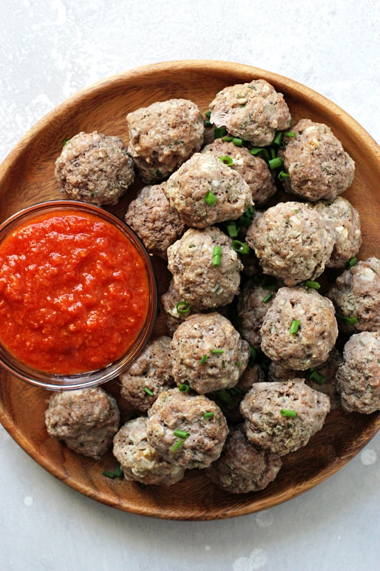 A wooden plate with Dairy Free Meatballs and a bowl of marinara sauce.