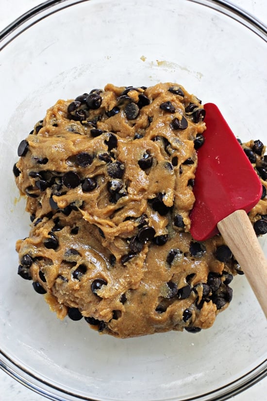 A glass mixing bowl filled with cookie dough and a spatula.