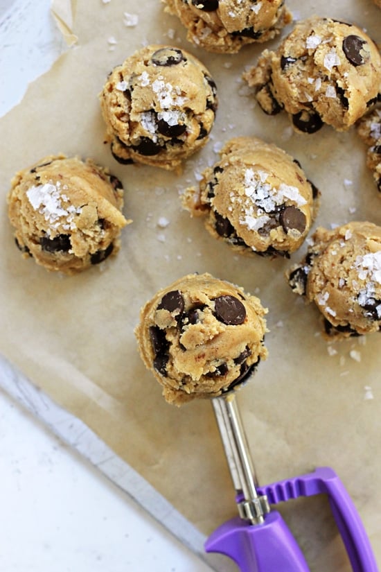 A cookie scoop and cookie dough balls on a baking sheet.