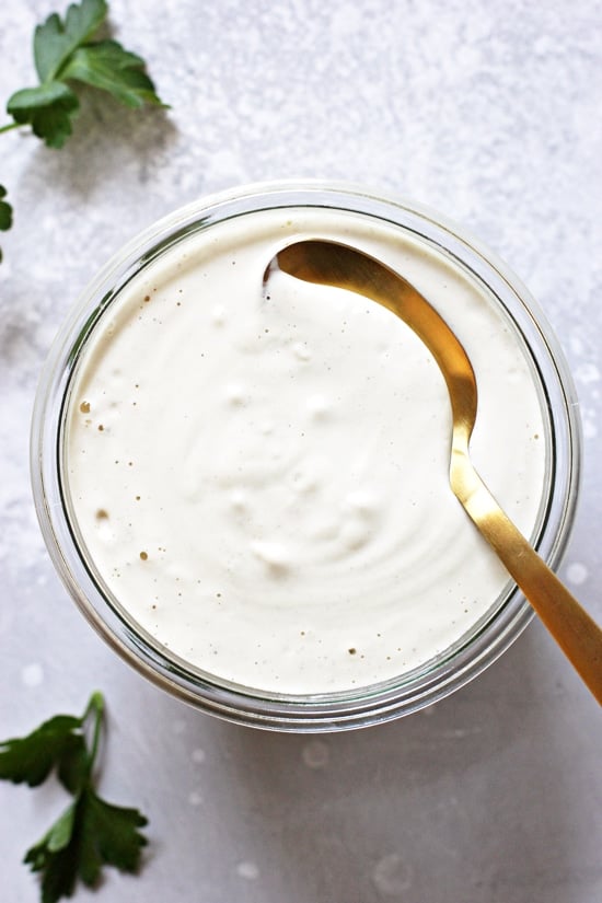 A glass jar filled with Dairy Free Alfredo Sauce and a gold spoon.
