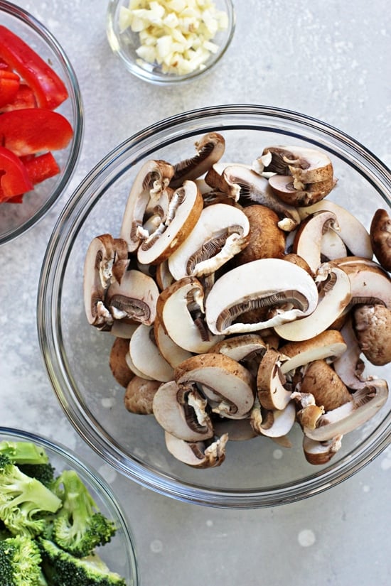 Glass bowls filled with sliced mushrooms, bell pepper and broccoli florets.