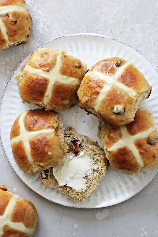 A white plate filled with Dairy Free Hot Cross Buns with one split open.