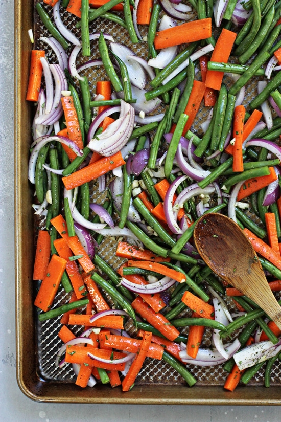 Uncooked veggies on a baking sheet with a wooden spoon.