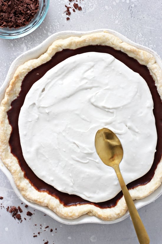 A pie with whipped topping being spread on with a spoon.