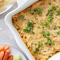 Dairy Free Buffalo Chicken Dip in a baking dish with chips & veggies to the side.