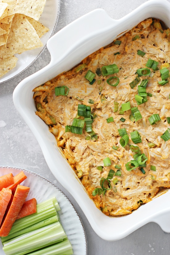 Dairy Free Buffalo Chicken Dip in a baking dish with chips & veggies to the side.
