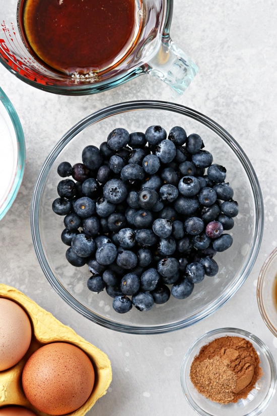 Fresh blueberries, eggs, coconut milk and maple syrup in small bowls.