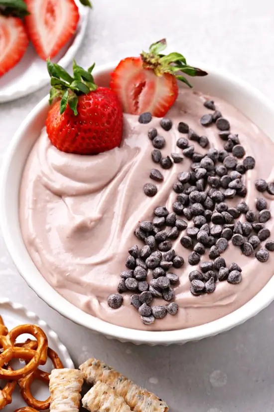 A bowl of Vegan Fruit Dip with two strawberries in the dish.