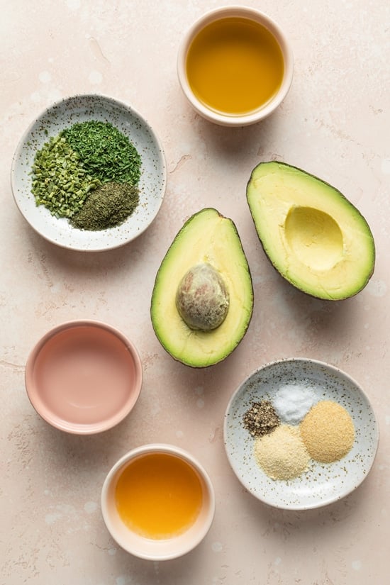 An open avocado, spices and oil in small bowls.