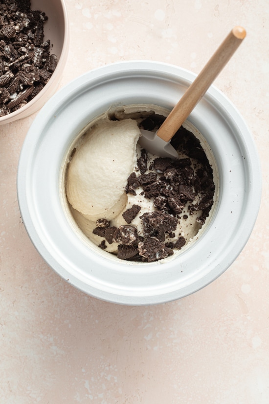 Ice cream in an ice cream maker with cookie crumbles on top.