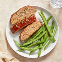 Three slices of Dairy Free Meatloaf on a plate with green beans.