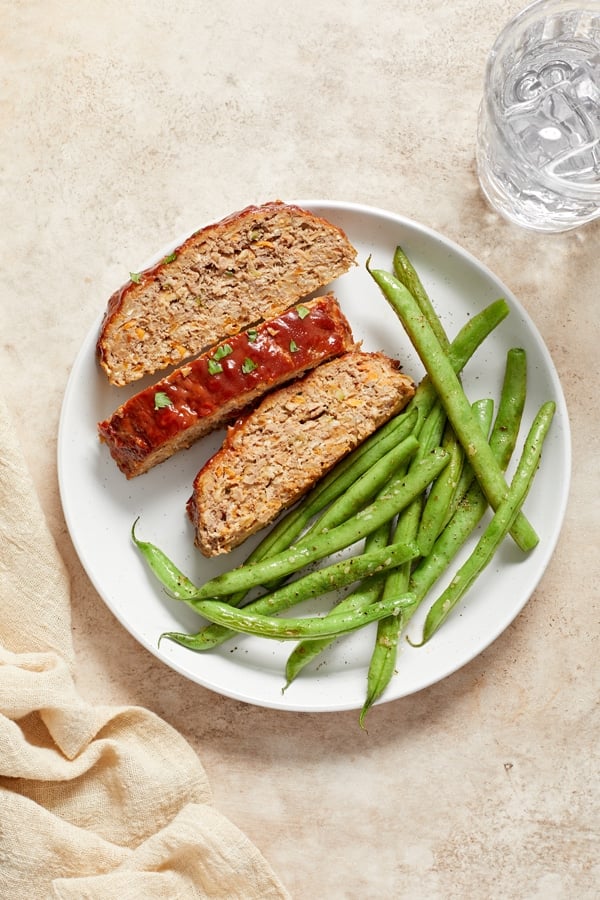 Three slices of Dairy Free Meatloaf on a plate with green beans.