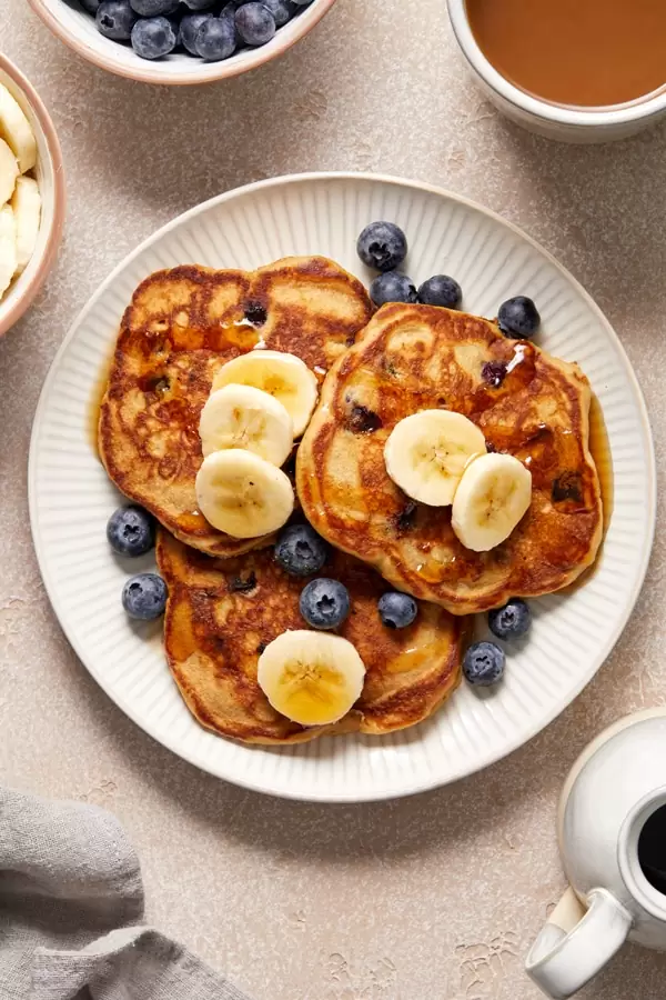 Three Dairy Free Oat Milk Pancakes on a plate topped with berries and banana.