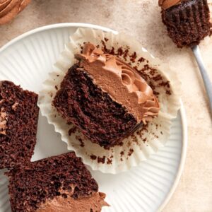 Several Dairy Free Chocolate Cupcakes with some split in half on a plate.