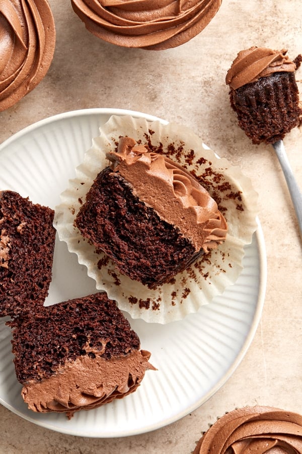 Several Dairy Free Chocolate Cupcakes with some split in half on a plate.