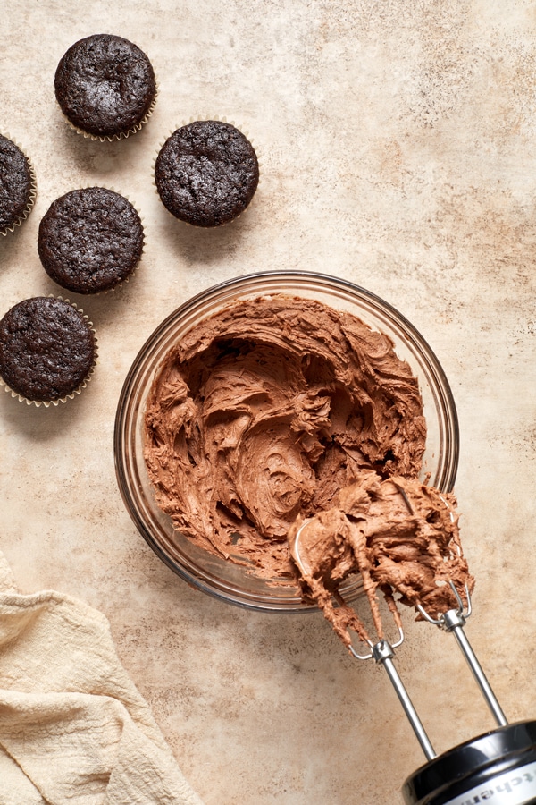 Dairy Free Chocolate Frosting in a mixing bowl with unfrosted cupcakes to the side.
