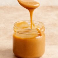 A jar of Dairy Free Caramel Sauce with some being drizzled with a spoon.