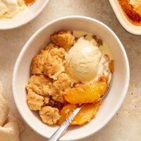 A bowl of Dairy Free Peach Cobbler topped with melted vanilla ice cream.