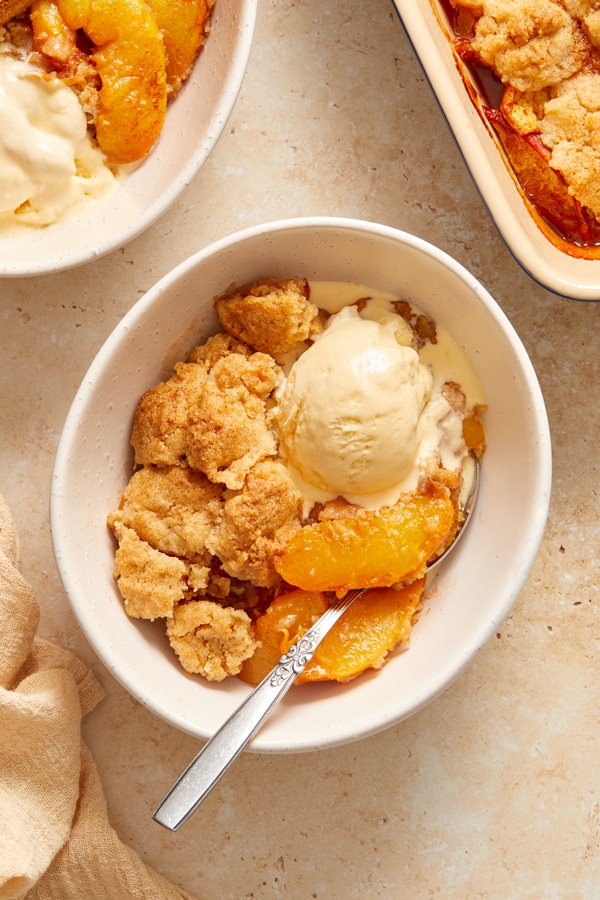 A bowl of Dairy Free Peach Cobbler topped with melted vanilla ice cream.