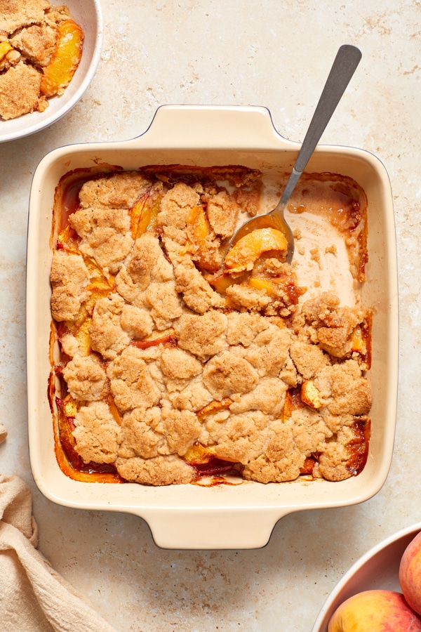 A Lactose Free Peach Cobbler in the baking dish with some scooped out with a spoon.