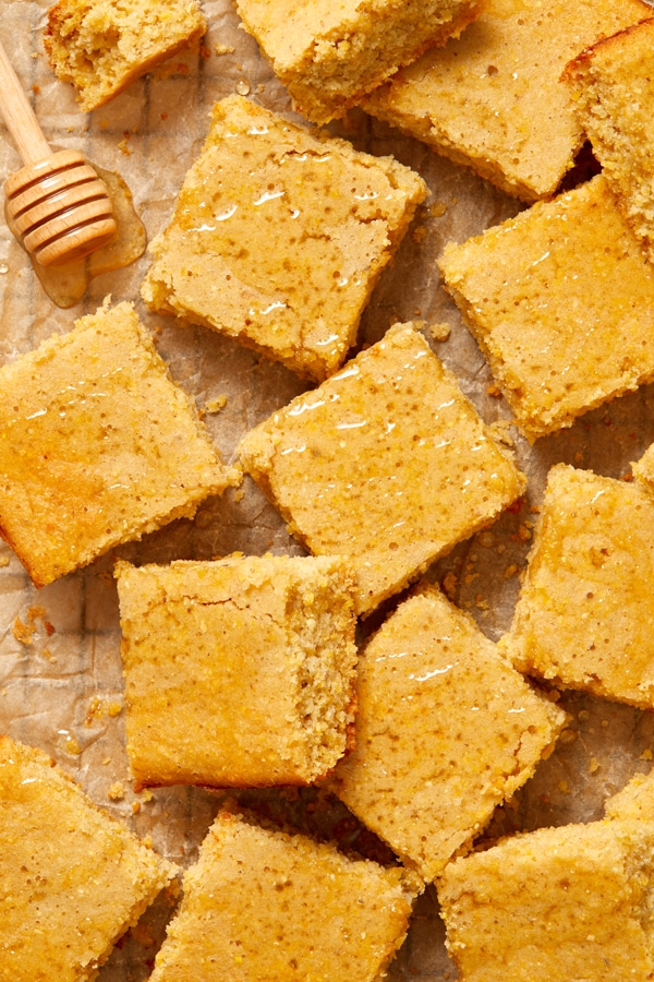 Slices of Dairy Free Cornbread on parchment paper drizzled with honey.