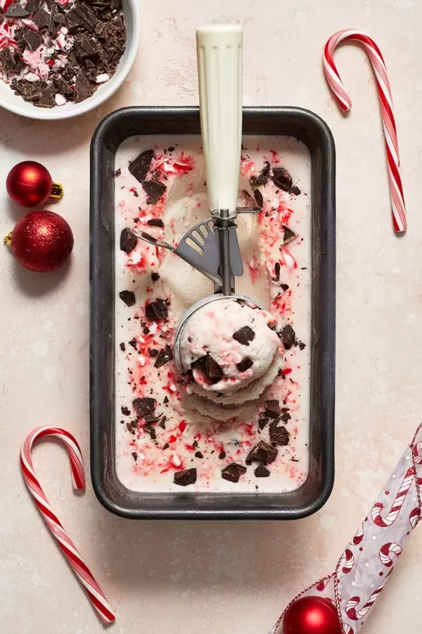 A loaf pan filled with Dairy Free Peppermint Bark Ice Cream and a scooper.